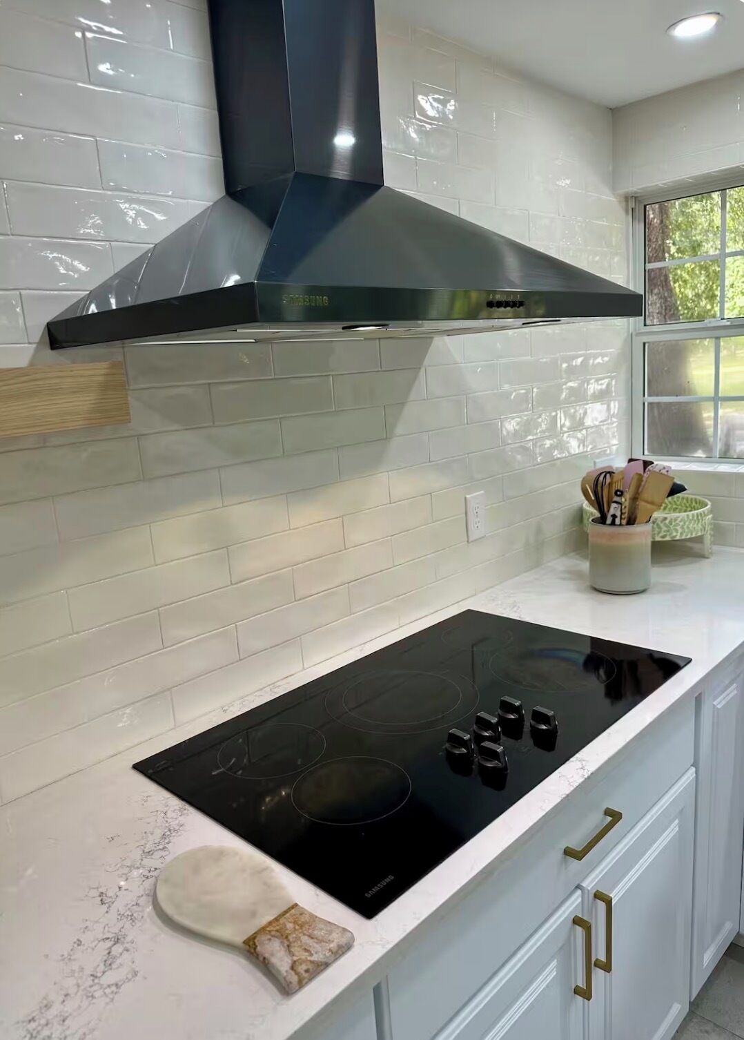 A kitchen with a black induction cooktop, white cabinets, and a stainless steel range hood.