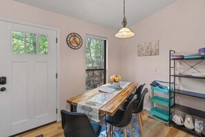 A dining area with a wooden table, chairs, a clock, and a window with a view of trees. - Rustic 2BR Cabin *POOL* Wooded (Kimberling City)