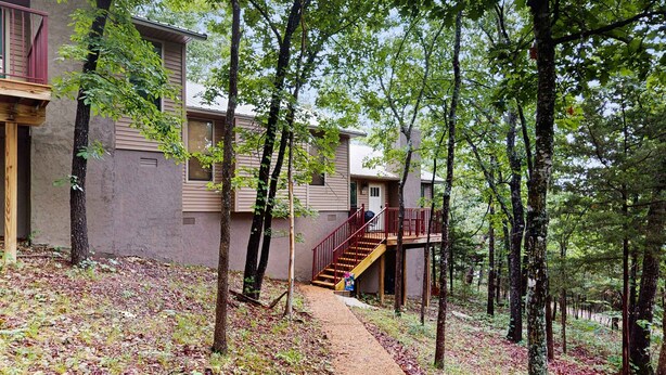 A building with a wooden staircase leading to a balcony, surrounded by trees. - Rustic 2BR Cabin *POOL* Wooded (Kimberling City)