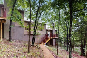 A building with a wooden staircase leading to a balcony, surrounded by trees. - Rustic 2BR Cabin *POOL* Wooded (Kimberling City)