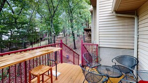 A wooden deck with metal chairs and a table, surrounded by a red railing, overlooking a forested area. - Rustic 2BR Cabin *POOL* Wooded (Kimberling City)