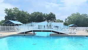 A swimming pool with a white fence and a bridge, surrounded by trees and covered structures. - Rustic 2BR Cabin *POOL* Wooded (Kimberling City)