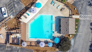 Vista aerea di una zona piscina con piscina rettangolare, lettini, ombrelloni e un piccolo edificio.