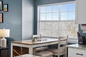 A kitchen with a dining table, chairs, a window with blinds, a lamp, and kitchen utensils. - 2BR Eagles Nest Condo - MOUNTAIN VIEWS - Pool (Branson)