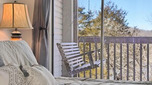 Una camera da letto con un letto, una sedia, una lampada e vista alberi attraverso la ringhiera del balcone.