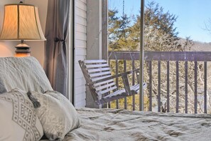 A bedroom with a bed, a chair, a lamp, and a view of trees through a balcony railing. - 2BR Eagles Nest Condo - MOUNTAIN VIEWS - Pool (Branson)