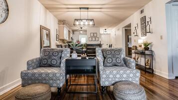 A modern living room with patterned sofas, a coffee table, and a dining area with a chandelier.