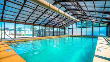 An indoor swimming pool with clear blue water, a metal roof, and a view of the outside.