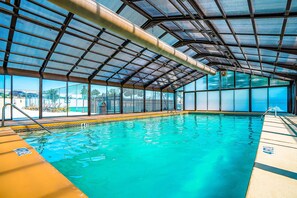 An indoor swimming pool with clear blue water, a metal roof, and a view of the outside. - Ground-Floor 2BR # POOL & GOLF # Pet Friendly (Branson)