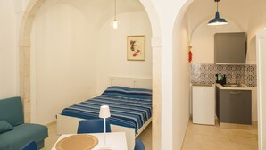A room with a bed, a desk, a chair, a small kitchenette, and an arched doorway. - Southeast 13 - Moon House (Putignano)