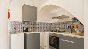 A compact kitchen with a refrigerator, oven, and dishwasher, featuring a patterned backsplash and arched ceiling. - Southeast 13 - Moon House (Putignano)