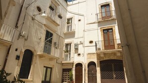 A narrow street with buildings featuring balconies, arched doorways, and a small garden area. - Southeast 13 - Moon House (Putignano)