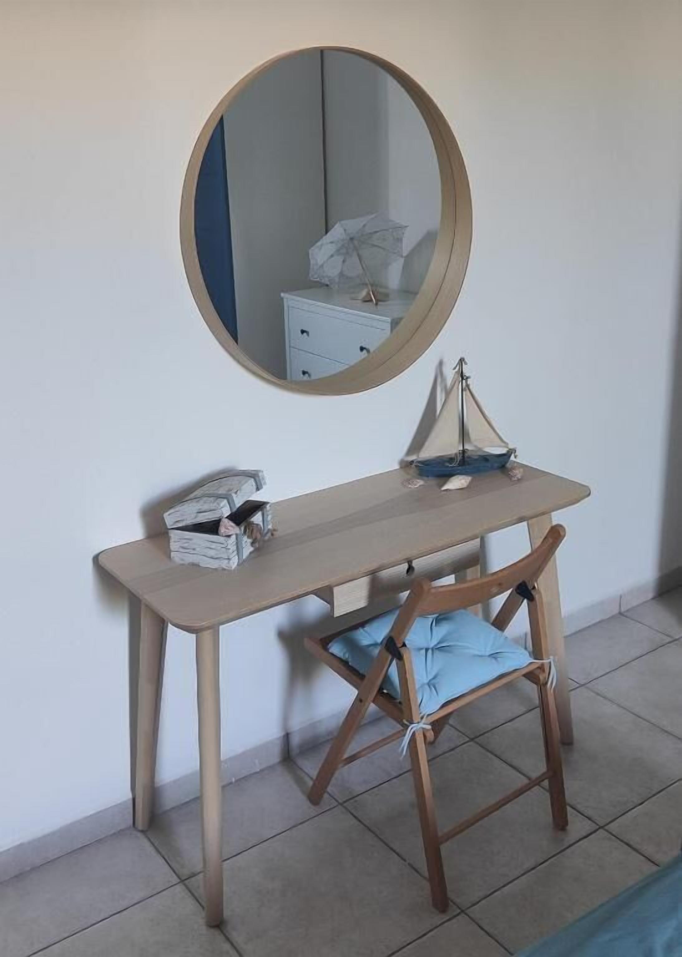 A small desk with a mirror, a chair, and a small table with a sailboat model.