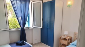 Een kleine, net kamer met twee bedden, een raam met gordijnen, een bureau met lamp en een garderobe.