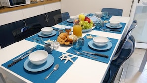 Een eettafel gedekt met borden, bestek en een schaal fruit.