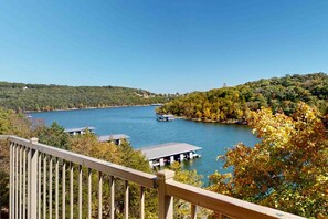 Vista sul lago con una terrazza in legno che si affaccia sull'acqua, barche ormeggiate e edifici sulla riva.