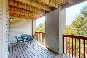 Eine Holzterrasse mit Tisch und Stühlen, eine Betonstütze und Blick auf Bäume.