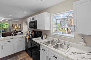 A modern kitchen with white cabinetry, a black stove, and a large window with a 'hello' sign. - Serene 2BR Condo - Ozark views - Pool & Hot Tub (Branson)
