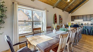 Ein Essbereich mit Holztisch und -stühlen, ein Fenster mit Blick auf ein Haus und eine Küche im Hintergrund.