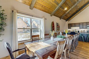Ein Essbereich mit Holztisch und -stühlen, ein Fenster mit Blick auf ein Haus und eine Küche im Hintergrund.