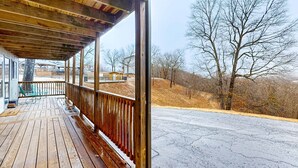 Une terrasse en bois avec un banc, une rambarde et une vue sur un paysage aride, parsemé d’arbres et de collines.