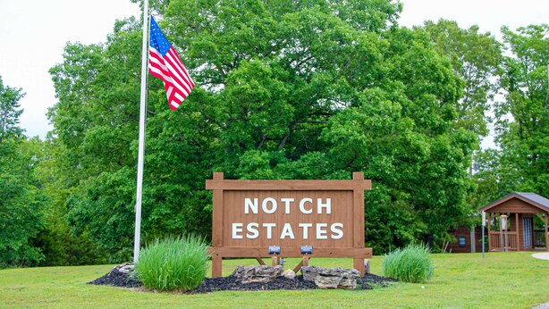 Un panneau en bois sur lequel on peut lire « NOTCH ESTATES », entouré de verdure et surmonté d’un drapeau.