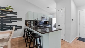 Een moderne keuken met een centraal kookeiland, barstoelen, een magnetron en een koelkast.