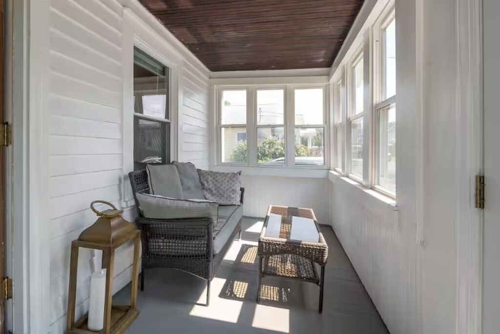 A sunroom with a sofa, wicker chairs, a table, and a lantern.
