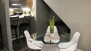 Et spiseområde med et glasbord, hvide stole og en potteplante.