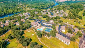 Ovenfra ses et boligområde med huse, en swimmingpool, tennisbaner og en flod.