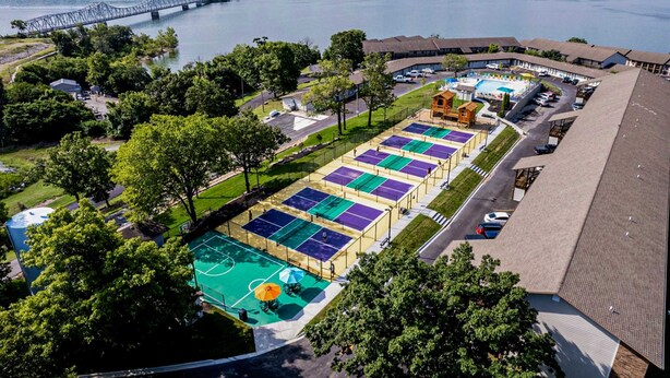 Luchtbeeld van een hotel met een groot sportterrein, een zwembad en een brug op de achtergrond.