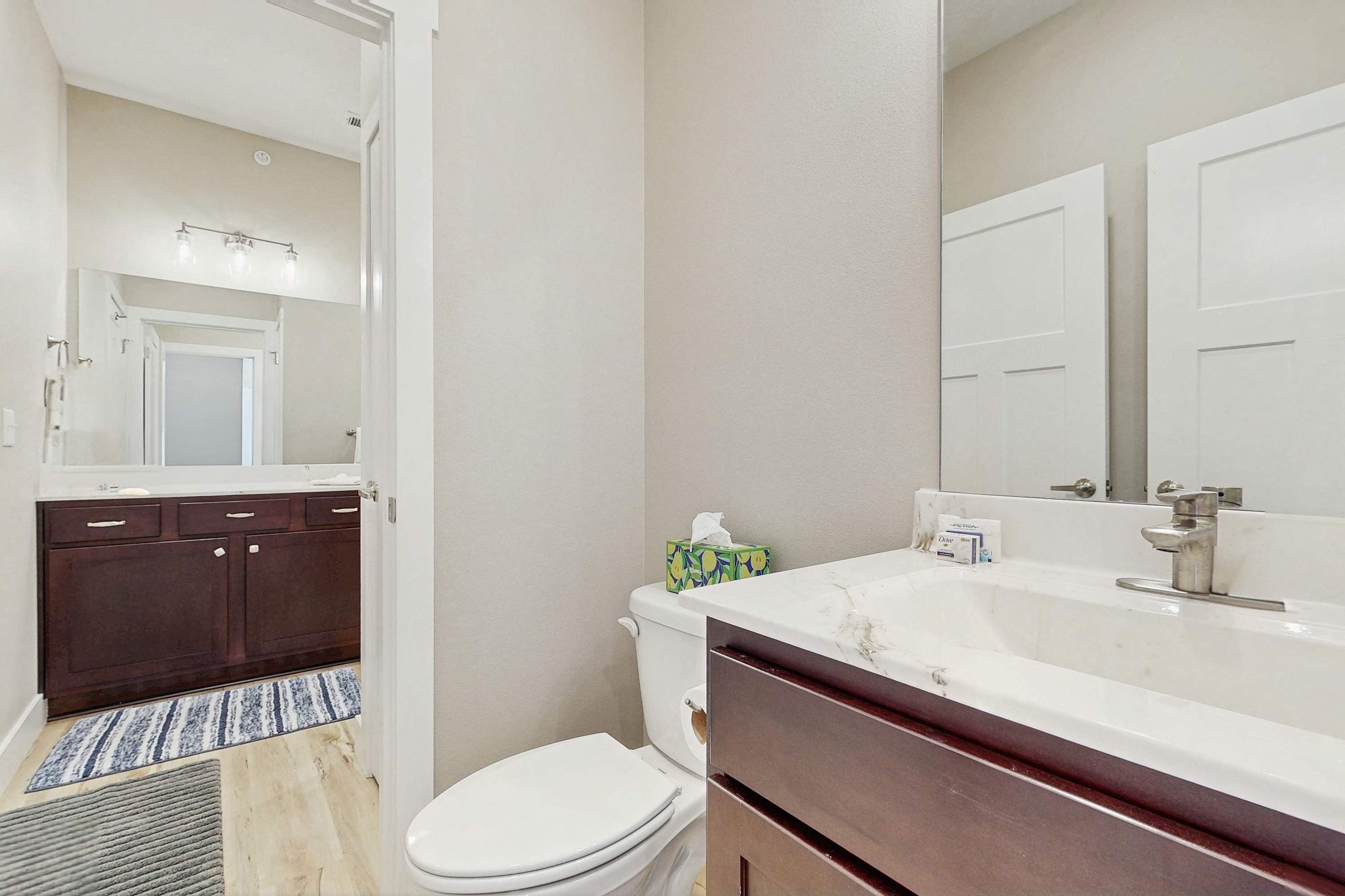 A bathroom with a white toilet, dark wooden cabinets, a white sink with a mirror, and a light-colored floor.