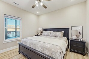 Quarto com cama, mesas de cabeceira, ventilador de teto, janela com vista e quadro na parede.