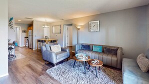 A modern living room with a grey sofa, a coffee table, and a dining area with a table and chairs. - Warm 3BR Condo - MOUNTAIN VIEWS - COMMUNITY POOL (Branson)