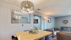 A dining area with a wooden table, chairs, a chandelier, a mirror, and a wall with a light fixture and a decorative wreath. - Warm 3BR Condo - MOUNTAIN VIEWS - COMMUNITY POOL (Branson)