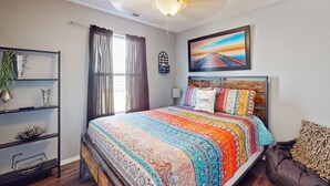 A bedroom with a bed, a ceiling fan, a window with curtains, a shelf with decorative items, and a painting on the wall. - Warm 3BR Condo - MOUNTAIN VIEWS - COMMUNITY POOL (Branson)