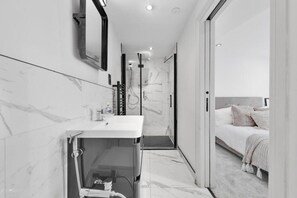 A modern bathroom with a marble vanity, a shower, and a bedroom with a bed and a nightstand. - Luxury 2 Bedrooms 2 Bath London Flat 6 Guests (London)