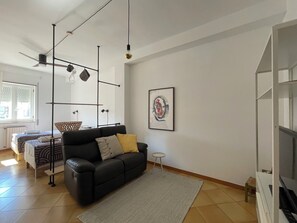 A modern living room with a black sofa, a small round table, and a framed abstract painting on the wall. - Ostuni Home with Terrace & Free Parking – Near Old Town (Ostuni)