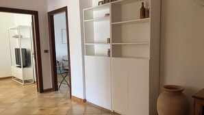 Una stanza con un armadio bianco, un vaso grande e un televisore in un angolo.