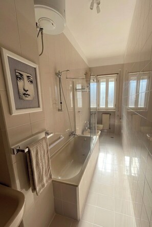A modern bathroom with a large bathtub, a glass shower enclosure, and a window providing natural light. - Ostuni Home with Terrace & Free Parking – Near Old Town (Ostuni)