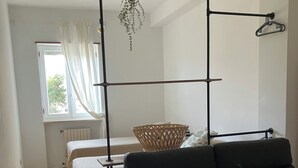 Una stanza con un divano in pelle nera, un letto con testiera bianca, una pianta pensile e una finestra con tende.