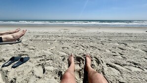 Ein Strand mit Sand und Fußspuren, Füße und Flip-Flops.
