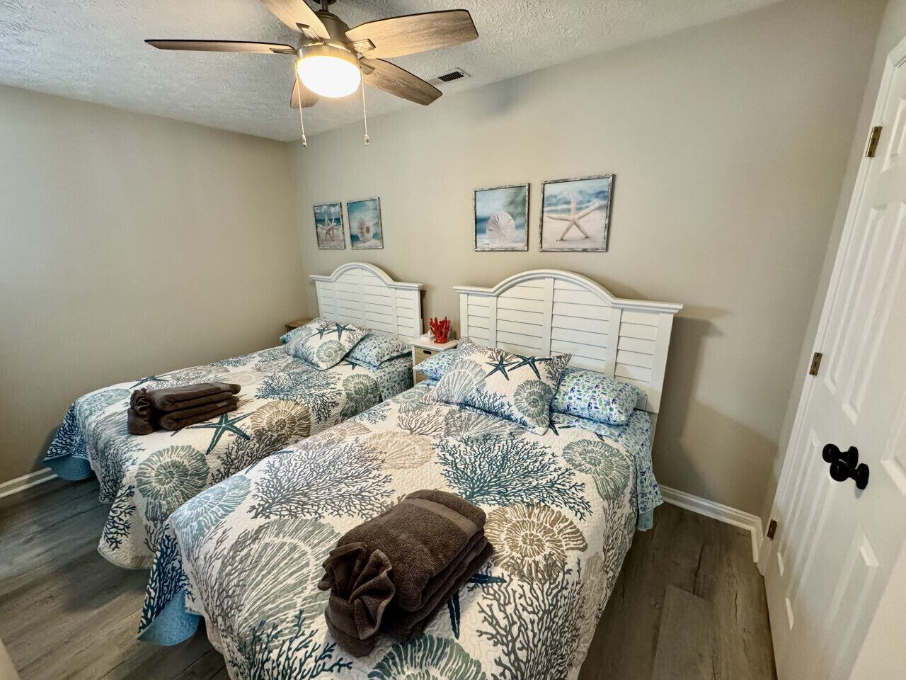 A bedroom with two beds, a ceiling fan, and artwork on the wall.