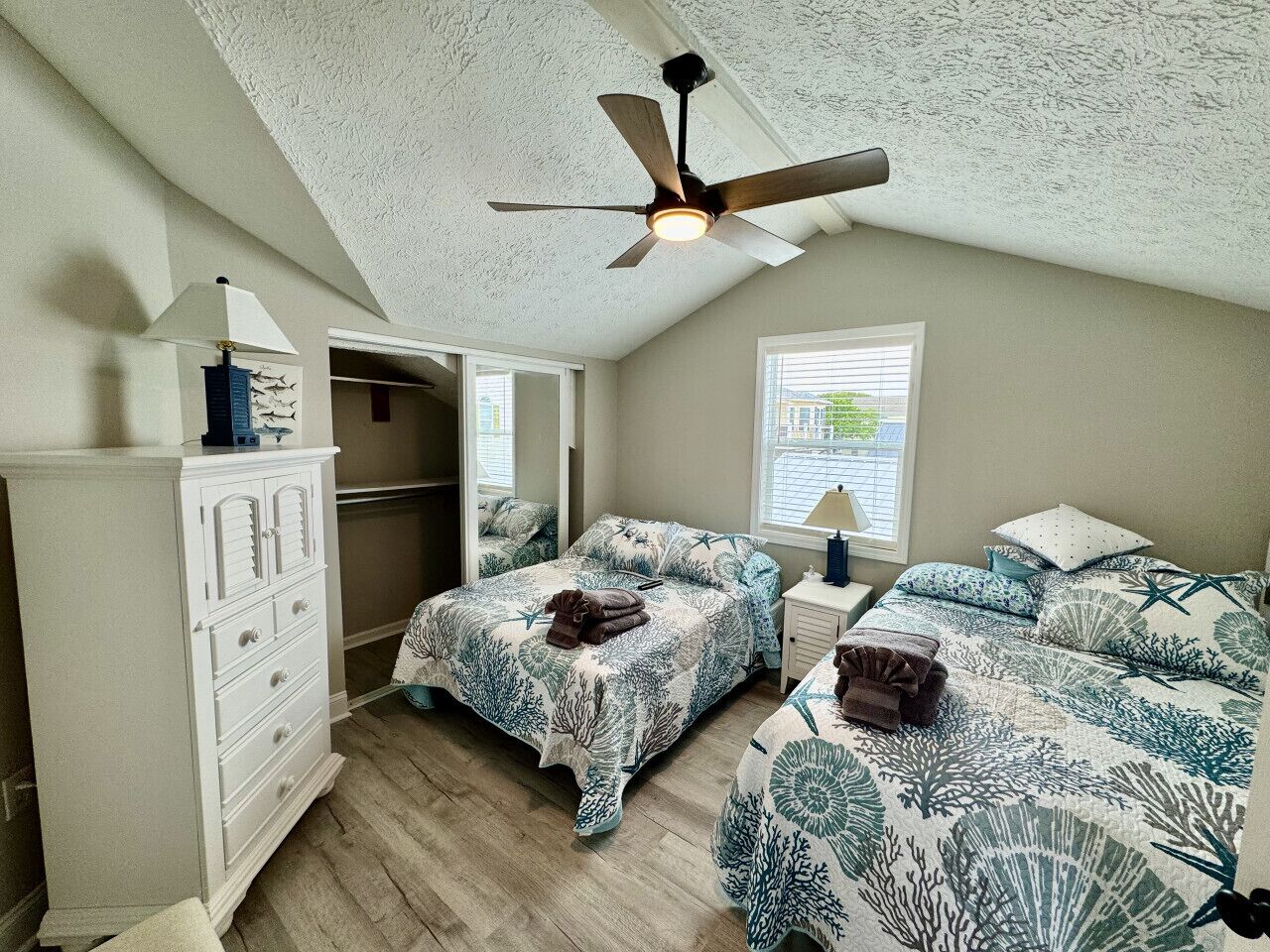 A bedroom with two beds, a ceiling fan, a walk-in closet, and a window with blinds.