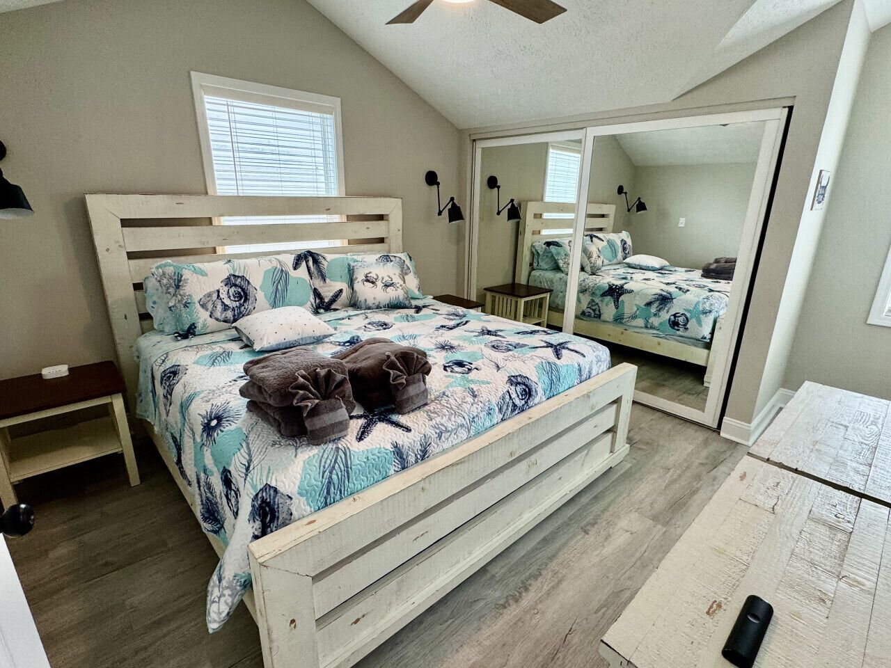 Quarto com cama, mesa de cabeceira, espelho e ventilador de teto.