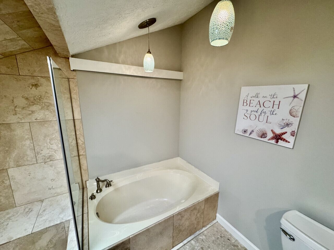 Ein Badezimmer mit freistehender Badewanne, einer Duschkabine aus Glas, einer Wandleuchte und einem dekorativen Schild.