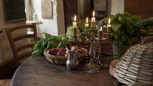Une table à manger rustique, agrémentée d’un chandelier à bougies, de légumes frais et d’un panier en osier.