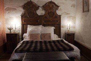 A bedroom with a wooden headboard, a bed with white linens, a fur throw, and two bedside tables with candles.