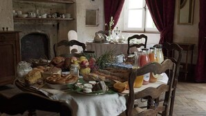 Une salle à manger traditionnelle avec une table en bois mise pour le petit-déjeuner, où l’on trouve du pain, des viennoiseries, des fruits et des boissons.