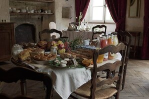 A traditional dining room with a wooden table set for breakfast, featuring bread, pastries, fruits, and beverages.